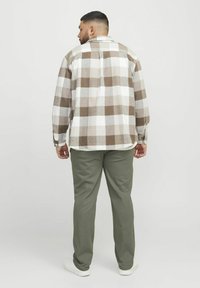 Geverfde katoenen overhemd in beige en bruine tinten, met lange mouwen en een relaxte pasvorm, gedragen met olijfgroene broek en witte sneakers.