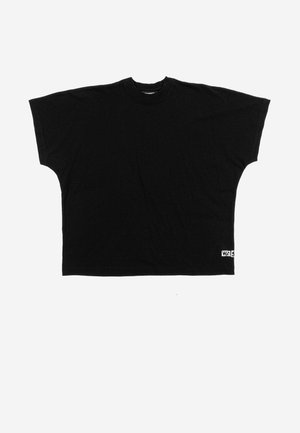 Svart oversized T-skjorte med korte ermer og rund hals, løs passform og en liten hvit lapp med svart tekst på nederste høyre kant.