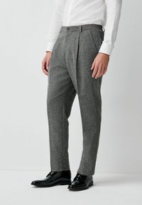 Gray plaid trousers with a tailored fit, pleated front, and belt loops, paired with polished black shoes. Smooth wool blend texture.