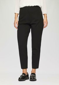 Zwarte op maat gemaakte broeken met een hoge taille, pin-tuck details en taps toelopende benen, gemaakt van gladde stof. Gecombineerd met glanzende zwarte instappers.