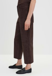 Braune Wildleder-Hosen mit weitem Bein und hoher Taille, mit einem Knopfverschluss und einer glatten Textur. Kombiniert mit schwarzen Leder-Loafern.