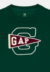 Mörkgrön babyhoodie med vit kontur av bokstaven "G" och en vinröd vimpelpatch med texten "GAP" över bröstet.