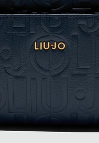 Granatowa torba skórzana o teksturowanej powierzchni z wytłoczonymi okrągłymi wzorami oraz złotym logo "LIU JO". Elegancki design z gładkim wykończeniem.