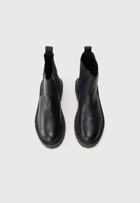 O pereche de botine Chelsea negre din piele, cu panouri laterale elastice și bucle de tragere, văzute de sus pe un fundal alb.