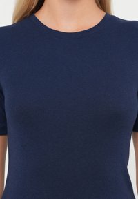 Mörkblå tight t-shirt med rund hals och korta ärmar, tillverkad av mjukt, elastiskt tyg. Inga synliga mönster eller detaljer.