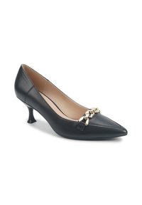 Zapato de tacón alto de cuero negro con punta afilada, que presenta un acento de cadena dorada en la parte frontal y un diseño de tacón curvado.
