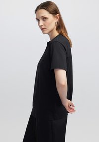 Camiseta negra de manga corta en suave tela de algodón. Presenta un cuello redondo clásico y un corte holgado, sin patrones ni acentos visibles.