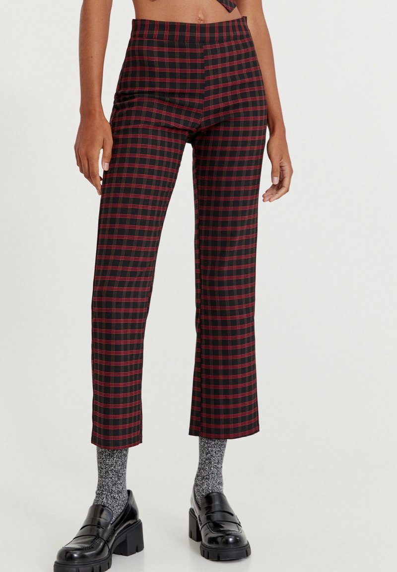 Zwart-rode geruite broeken met een hoge taille, cropped lengte en textuurstof. Gekoeld met grijze sokken en stevige zwarte schoenen.