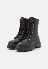 Černé kožené kotníkové boty s texturovaným povrchem, kulatou špičkou a silnou platformou. Obsahují kovové očka a černé tkaničky.
