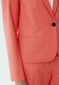 Koraalkleurig colbert met één zwarte knoop, slim fit en een gladde textuur. Heeft een rechte zakdesign en lange mouwen.