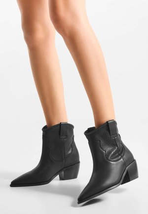 Čierne kožené členkové topánky so špicatou špičkou, textúrovanými perforovanými akcentmi a nízkym širokým podpätkom, s prešívanými detailmi pozdĺž bokov.