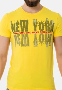 Gelbes Baumwoll-T-Shirt mit grafischem Text "NEW YORK" in Schwarz mit roten Akzenten, kurzen Ärmeln und einem runden Halsausschnitt.