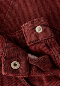 Gros plan sur un tissu en denim rouge montrant deux boutons-pression en métal avec des motifs d'étoile sur des rabats cousus.
