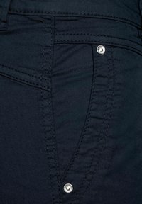 Mörkblå jeans med en närbild av tygtexturen, subtila sömmar och en metallknappaccent nära en ficka.