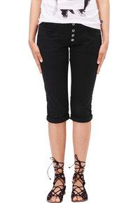 Los pantalones capri negros presentan un diseño ajustado con dobladillos enrollados, cinco bolsillos y acentos de botón metálico en la tapa frontal.