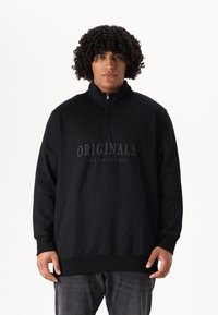 Crna dukserica na zip, s visokim ovratnikom, koja ima prednji kenguru džep i "ORIGINALS JACK & JONES" logo u mat završnici.