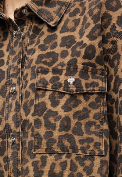 Close-up of a brown leopard print fabric shirt with a front buttoned chest pocket and dark buttons.