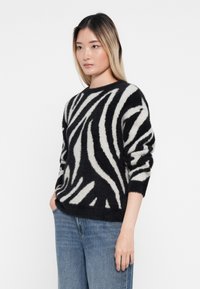 Sort-hvid stribet sweater med en blød, fyldig tekstur, rund halsudskæring og lange ærmer. Båret med blå denimjeans.