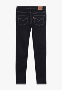 Jeans de mezclilla azul oscuro con un ajuste slim, que cuentan con bolsillos traseros distintivos con costuras curvas y detalles de costura amarilla en contraste.