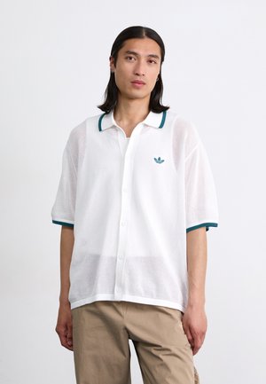 Biała siatkowa koszulka polo z akcentami w kolorze teal na kołnierzyku, z guzikami z przodu i małym zielonym logo na lewej piersi. Lekki i teksturowany materiał.