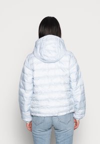 Világoskék pufferek jackets kapucnival, steppelt textúrával, rugalmas mandzsettákkal és húzózsinóros alsó résszel. Simasága miatt fényes felület jellemzi.