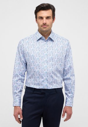 Weißes Hemd mit Knöpfen und einem Blau-Grün-Blattmuster, langen Ärmeln und klassischem Kragen, kombiniert mit dunkelblauen Hosen.