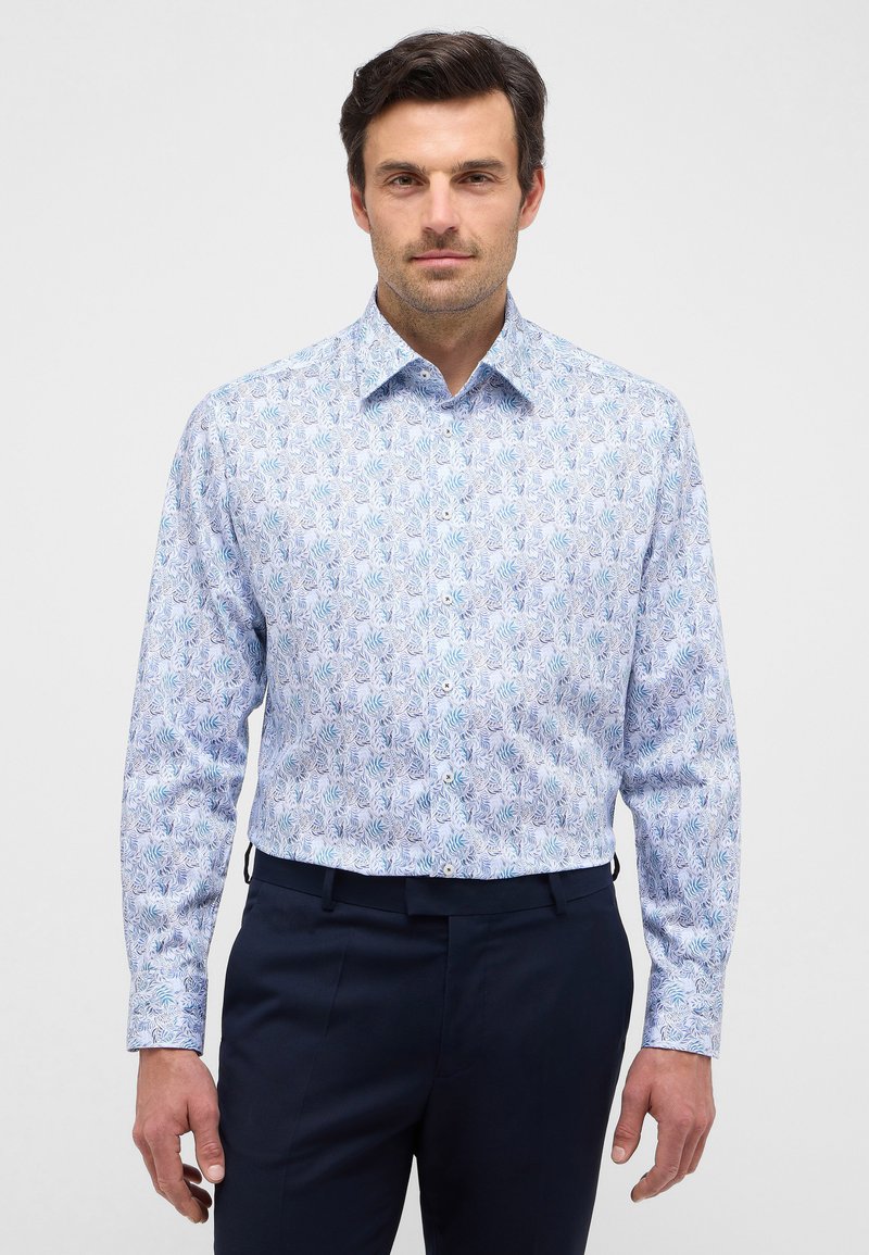 Camicia bianca con un motivo a foglie blu e verdi, maniche lunghe e colletto classico, abbinata a pantaloni blu navy.