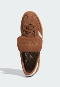 Hnedé semišové tenisky s textúrovanými koženými akcentmi, šnúrkami a polstrovaným jazykom. Majú biely pruh a vzorovanú stielku.