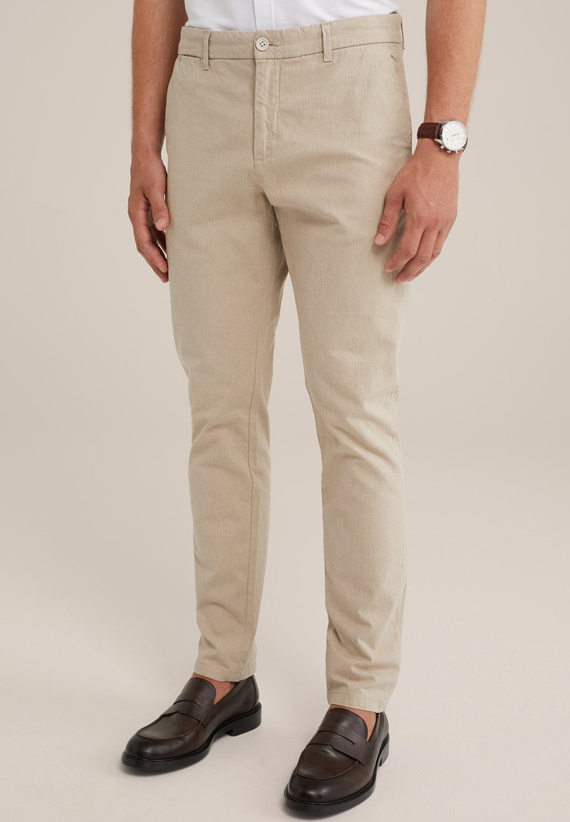 Pantalones de mezcla de algodón beige con un corte slim, presentan un corte recto, bolsillos frontales y un cierre de botón único. Combinados con mocasines oscuros.