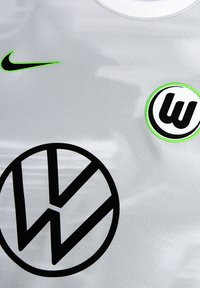 Grijze sporttrui van textuurstof, met een zwart Volkswagen-logo en een cirkelvormig groen en zwart Wolfsburg-embleem, voorzien van een Nike-swoosh.