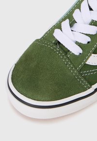Sneaker en daim vert avec un bout en daim, des coutures blanches, des lacets blancs et une semelle en caoutchouc blanche avec une rayure noire sur fond blanc.