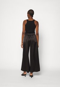 Svart ribbad tanktopp parat med flödande svarta satinvidebyxor, med elastisk midja och slät textur. Minimalistiska skor fulländar looken.