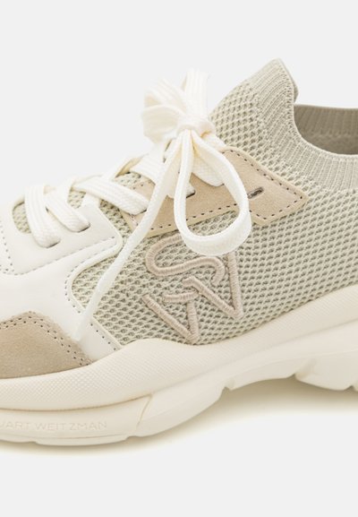 Sneaker featuring a mesh upper in light gray, suede accents, cream laces, and a textured sole with embossed branding on the side.