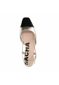 Gouden metallic hoge hak schoen met zwarte cap toe, slanke enkelriem en beige binnenzool met 'SACHA' branding. Gladde textuur.
