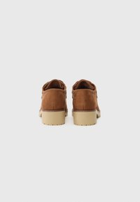 Chaussures en daim marron avec une semelle beige plate, au design arrondi et à la finition minimale, mettant en valeur une texture lisse et une structure simple.