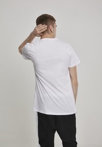 Balti trumpa rankovėmis t-shirt, pagaminta iš švelnaus medvilnės, su apvalia iškirpte, lygi tekstūra ir atsipalaidavusiu siluetu, rodoma iš nugaros.