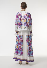 Floral-patterned silk blouse and skirt set featuring vibrant colors, a flowing design, and ruffled cuffs, with blue and purple accents.
