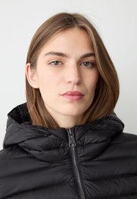 Giacca a vento nera con colletto alto e design leggero e trapuntato. Il dettaglio della cerniera è evidente, migliorando il suo aspetto elegante.