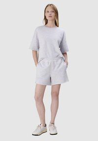 Jasnoszary bawełniany t-shirt z krótkimi rękawami w zestawie z pasującymi szortami. Strój ma elastyczną talię i luźny krój. W komplecie białe sneakersy.