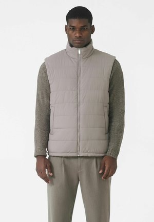 Gray puffer vest with high collar, zip closure, and quilted pattern. Worn over a textured dark gray sweater. Simple, streamlined design.