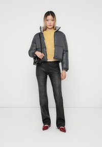 Grå puffjakke med cropped design og leopardmønsteret foring, kombinert med en gul strikkegenser og svarte jeans. Røde sko og en svart håndveske.