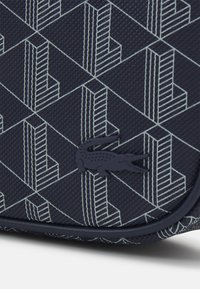Tessuto blu navy con una texture che presenta un motivo geometrico in grigio chiaro. Include un accento logo scuro. Design compatto con linee pulite.