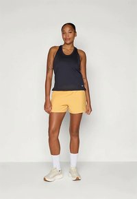 Mustat topit ja keltaiset shortsit. Yläosa on racerback-mallia; shortsit ovat rentoa mallia. Yhdistetty valkoisten sukkien ja vaaleiden lenkkarien kanssa.