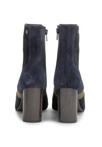 Botas de ante negro y azul marino con un tacón de madera ancho. Presentan un cierre de cremallera y una banda de acento verde oliva alrededor del mediopie.