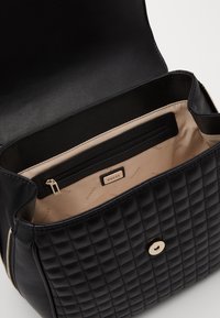 Mustat päällysteiset keinonahkaiset käsilaukut, joissa on kultasävyinen painonappi, sisätasku ja vaaleanbeige vuori. Laukussa on myös tuotemerkki sisäpuolella.