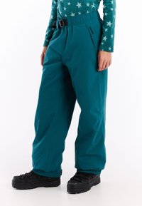 Tyrkysové sněhové kalhoty s elastickým pasem a pásem, s postranními kapsami a elastickými manžetami, spárované s černými zimními botami.