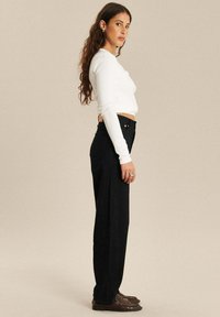 Zwarte high-waisted broek met een rechte snit, gecombineerd met een witte blouse met lange mouwen. Outfits hebben een eenvoudig ontwerp en een klassieke pasvorm.