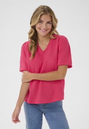 Blouse rose à manches courtes avec un col en V, motif texturé et dentelle aux manches, associée à un jean bleu. Fini en tissu lisse.