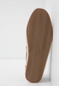 Semelle d'espadrille avec une semelle en caoutchouc marron ondulée, un dessus en jute naturel et des accents en tissu bleu sur les côtés.