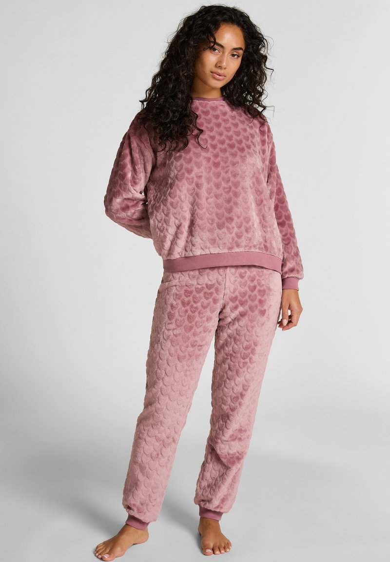 Miękki, strukturalny komplet dresowy w przykurzonym różu z wzorem w łuski. Sweter z okrągłym dekoltem oraz elastyczne spodnie z dopasowanymi mankietami.